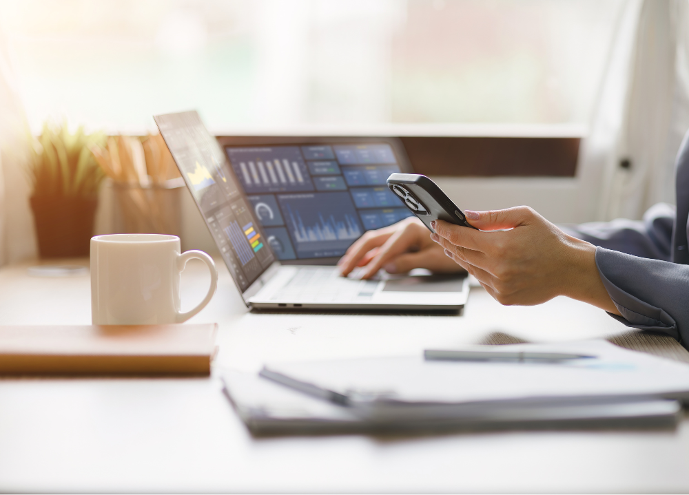 www.titicus.comhubfsWoman looking at phone while sitting at desk with laptop that has data on the screen